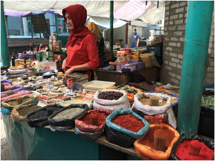 Marktfrau verkauft Gewürze, Kräuter und Trockenfrüchte an einem bunten Basarstand