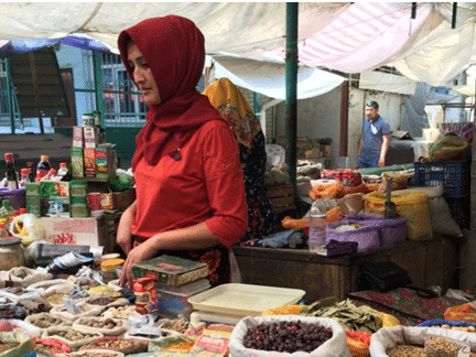 Market woman selling spices, herbs, and dried fruits at a colorful bazaar stall